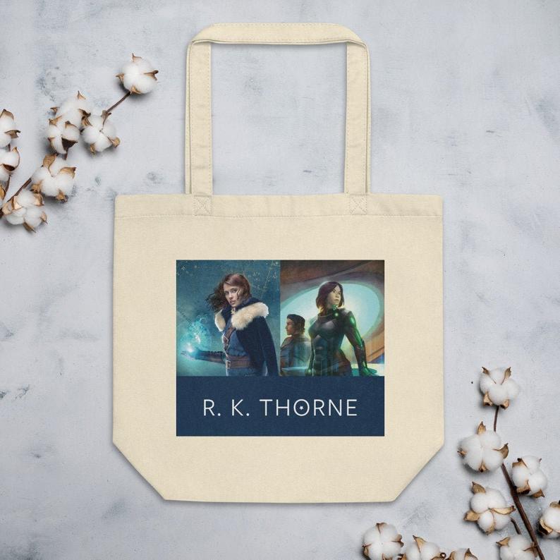 A beige eco tote bag with images from R.K. Thorne book covers featured on a gray background with some cotton plants