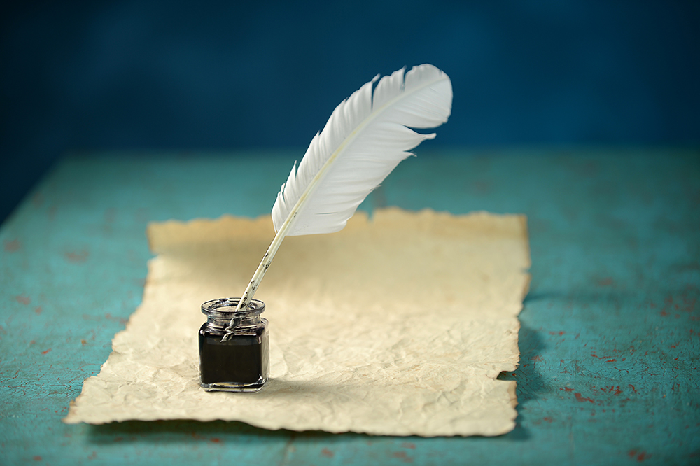 A bottle of ink and a quill set on a piece of parchment on a teal background.