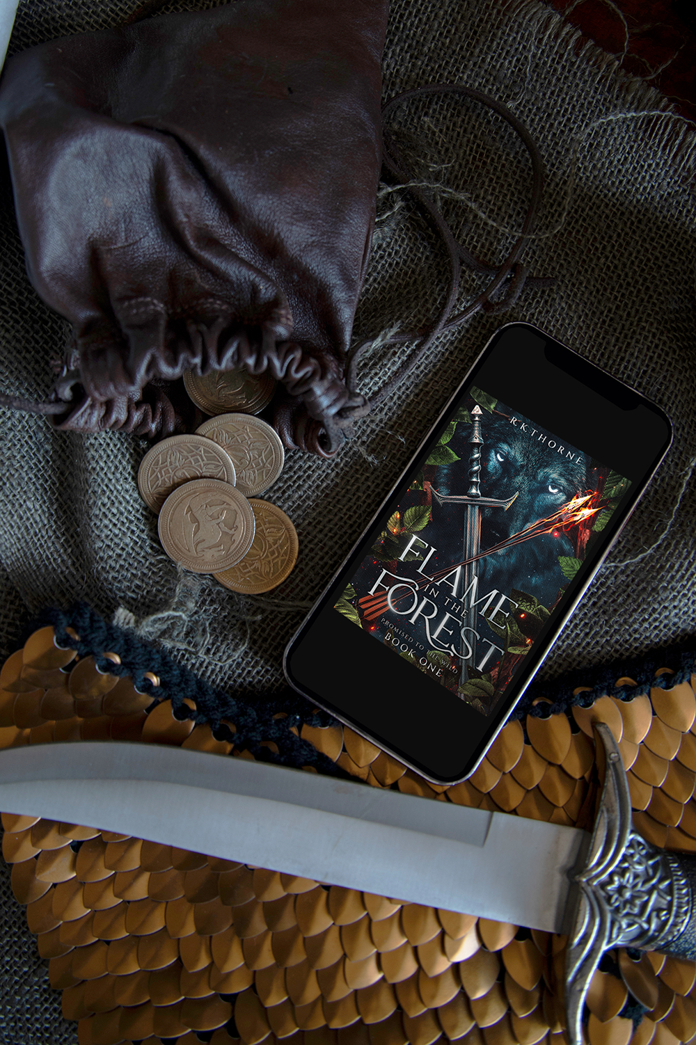 Cover of Flame in the Forest on a phone near a dagger and some coins